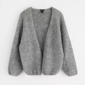 Grå stickad kofta - Mysig grå stickad kofta från Lindex  med djup v-ringning och långärmad modell. Koftan har en loose passform och är perfekt att slänga på sig när det är kyligt. Tillverkad i ett mjukt och fluffigt material som känns skönt mot huden. Storlek xs/s, helt ny!!!