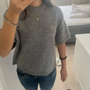 Grå stickad tröja från Gina Tricot - Mysig grå stickad tröja från Gina Tricot i ullblandning. Tröjan har korta ärmar, rund halsringning och en avslappnad passform. Helt ny med prislapp kvar, köpte för 300kr men kommer inte till användning 💞