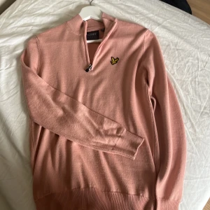 Rosa stickad half zip från Lyle & Scott - Säljer en rosa stickad tröja från Lyle & Scott i storlek S. Tröjan har half zip-dragkedja, lång ärm och klassisk gul logga på bröstet. Perfekt för dig som gillar stilren och bekväm design med en modern touch. Knappt använd.