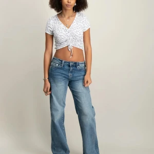 Vit croppad topp med snörning från RYVLS - Säljer en vit croppad topp från RYVLS med blått blommigt mönster och ribbad struktur🌊🌸. Toppen har v-ringning, korta ärmar och snygg snörning framtill som ger en cool look. Perfekt för dig som gillar trendiga och bekväma plagg. Går lätt att justera hur kort/lång man vill ha den🤩🌿Använd några få gånger men är i väldigt bra skick🪽💫🥰