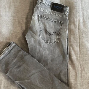 Replay grå slitna jeans - Grå jeans från Replay med slitningar och trasiga detaljer på benen för en cool, avslappnad look. Klassisk femficksmodell med svarta sömmar och Replay-logga på bakfickan. Jeansen är i denim och har en rak passform. Säljer pga att de är förstora hade haft kvar de om de passa, väldigt fint par med fett platina, jeansen har lagats vid skrevet innan annars är de i bra skick, Hör av er vid frågor osv😊