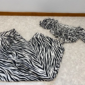 Zebramönstrad sett - Säljer en snygg zebramönstrad sett i svart och vitt. Settet har offshoulder-ärmar med resår och volangdetaljer, samt knyt i midjan. Perfekt för dig som vill sticka ut med ett djurmönster och trendig passform.