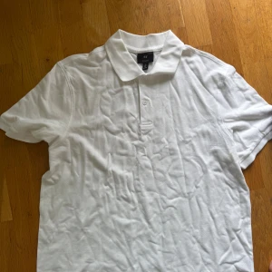 Vit pikétröja från H&M - Fräsch vit pikétröja från H&M med klassisk krage och två knappar framtill. Regular fit och tillverkad i mjuk bomull som är skön mot huden. Perfekt för en clean och enkel stil, passar till jeans eller shorts.
