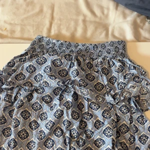 Blåmönstrad kortkjol från Gina Tricot - Supersöt blå kortkjol från Gina Tricot med elastisk smock i midjan och ett unikt mönster i olika blå nyanser. Kjolen är luftig och perfekt för varma dagar, och har en avslappnad passform som är lätt att styla med en enkel topp.