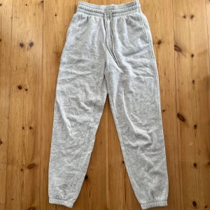 Grå mjukisbyxor från H&M - Grå mjukisbyxor från H&M i storlek XS. Byxorna har resår i midjan med snörning och muddar vid bensluten. Perfekta för chill dagar eller när du vill vara extra bekväm. Tillverkade i mjukt material som känns skönt mot huden. Skulle säga att de är midwaist men om man viker byxorna en gång blir de lågmidjade.