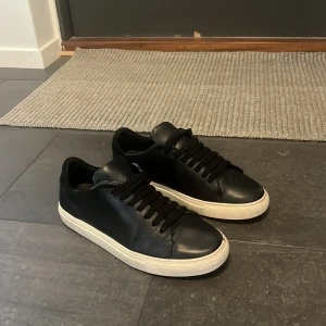 Arigato clean 90 - Stilrena svarta sneakers i skinn med klassisk vit sula och svarta snören. Lågt skaft och minimalistisk design som passar till det mesta. Perfekta för dig som gillar en clean look och vill ha ett par sneakers som funkar året runt. Har en liten defekt på höger sko (bild 4) annars i ett väldigt bra skick. Ny pris 2400, mitt pris 500. Priset kan diskuteras vid snabb affär! Skriv gärna vid frågor och funderingar 