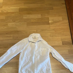 Vit skjorta - Klassisk vit skjorta från HM i bomull med lång ärm, bröstficka och knappar framtill. Skjortan har en rak passform och stilren krage, perfekt för en clean och enkel look.