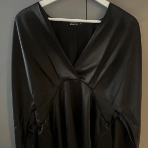 Svart långärmad satinblus  - Svart blus i satin från Gina Tricot. Blusen har v-ringning framtill, långa ärmar och markerad midja. 