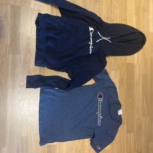 Champion - Snygg blå t-shirt från Champion med klassisk logga broderad på bröstet och en liten logga på ärmen. T-shirten har rund hals och korta ärmar, perfekt för en chill och sportig stil. Materialet känns mjukt och skönt mot huden. En mörk blå champion hoodie passar 12/14 år eller storleken S