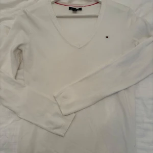 Vit v-ringad tröja Tommy Hilfiger XS - Klassisk vit v-ringad tröja från Tommy Hilfiger i mjuk bomull. Liten broderad logga på bröstet och ribbade muddar vid ärmslut och nederkant. Perfekt för lager-på-lager och enkel att matcha med allt.