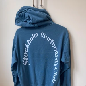 Stockhom surfboard club hoodie - Super snygg blå hoodie från stockholm surfboard club. Köpte den för några veckor sedan och har bara använts ett fåtal gånger den är som ny. Skriv för fler frågor eller funderingar. Har ej satt ett fast pris!