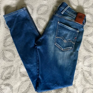 Replay Anbass - Snygga Replay Anbass jeans i klassisk blå tvätt med slitningar och ljusa detaljer. Modellen har raka ben, fem fickor och coola kontrastsömmar. Märkespatch i läder baktill och Replay-logga på fickan. Perfekta jeans för dig som gillar en populär och avslappnad stil.