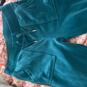 Turkosa juicy couture byxor - Säljer ett par turkosa mjukisbyxor från Juicy Couture. Byxorna har bred resår i midjan med snörning, stora fickor fram och bak med tryckknappar och broderad JC-logga. Brukar vika ner de för att få de ännu mer lågmidjade, skicka bilder på privat!