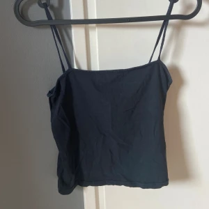 Svart enkel linnetopp - Säljer en svart, stilren linnetopp med smala axelband och rak halsringning. Toppen är croppad och sitter tight mot kroppen, perfekt till jeans eller kjol. Gjord i mjuk bomull som känns skön mot huden.