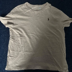 Beige t-shirt från Ralph Lauren - Säljer en stilren beige t-shirt från Ralph Lauren med klassisk rund hals och diskret logga broderad på bröstet. T-shirten är kortärmad och gjord i mjuk bomull, perfekt för en avslappnad look.