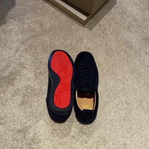  Christian Louboutin - Snygga mörkblå sneakers från Christian Louboutin med klassisk röd sula och ovandel i mocka. Skorna har rund tå, platt sula och snörning. Kommer med originalkartong, dustbag och äkthetskort. Perfekta för dig som vill sticka ut med exklusiv stil.
