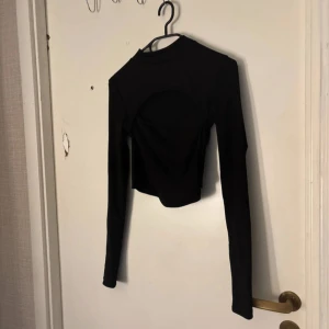 Svart croppad långärmad topp - Säljer en svart croppad topp med lång ärm och cool cut out-detalj över bröstet. Toppen har en tight passform och är perfekt för dig som vill sticka ut lite extra. Enkel att matcha med både jeans och kjol för en trendig look.