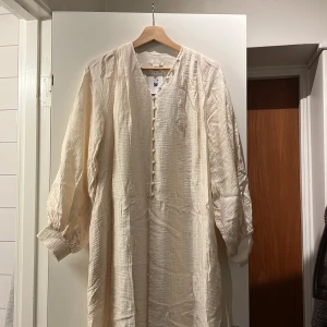 Ljus långklänning från H&M XS/S - Superfin ljus långklänning från H&M i luftig bomull. Klänningen har v-ringning, klädda knappar framtill och långa ärmar med breda muddar. Perfekt för dig som gillar en avslappnad men ändå stilren look. Kaftan.