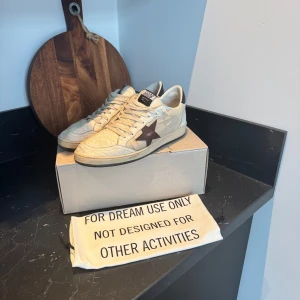 Golden Goose Ballstar - Säljer nu mina Golden Goose Ballstar i storlek 44! Kan möjligtvis även passa någon med storlek 45. Skorna är vita med detaljer i beige, en stjärna i brun/vinröd aktig färg och texten ”sneakers” i svart där bak. Kontakta mig vid frågor eller prisförslag! Kan även mötas upp i Kungsbacka/göteborg!