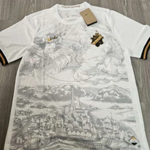 Vit AIK x Nike fotbollströja Stockholm - Snygg vit AIK fotbollströja från Nike med detaljer i svart och guld. Framsidan har ett unikt tryck med Stockholmsmotiv och klubbmärke på bröstet. Kortärmad modell med svarta och guldiga ränder på ärmsluten. Tillverkad i lätt och ventilerande material. Finns i både storlek S och M, vid frågor är det bara att höra av sig.