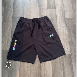 Svarta Under Armour shorts   ! L och M passar den ! - Svarta shorts från Under Armour i storlek XL med loose passform. Färgglad logga och text på sidan, elastisk midja med snörning. Perfekta för träning eller chill, tillverkade i mjuk polyester som andas. Snyggt sportig vibe med coola detaljer. De är Xl men på grund Thailand storlek blir den M L 