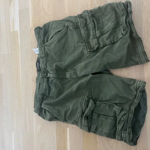 Gröna cargoshorts från On Our Terms - Snygga gröna cargoshorts från On Our Terms med flera praktiska fickor på sidorna och bak, perfekta för chill dagar. Shortsens material är mjuk bomull och de har en loose passform med klassisk midja. Stängs med knapp och dragkedja framtill.