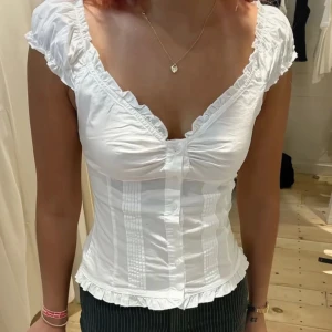 Brandy Melville topp - Supersöt vit korsettblus med volangkant vid ärmar och nederdel, v-ringning och knappar framtill. Från brandy melville så one size men det är väll en xs / s