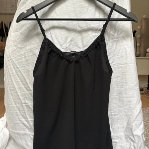 Svart spetslinne - Svart linne från Vero Moda i storlek XS. Linnet har tunna axelband och v-ringning med fina spetsdetaljer längs kanten. Materialet är lätt och faller snyggt, perfekt för en stilren look. Inga defekter!! Kontakta mig om du vill ha några funderingar!!❤️