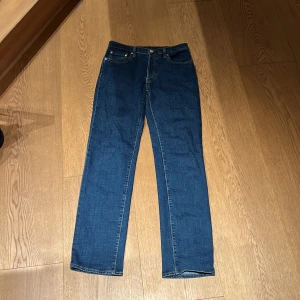 Levi's 501 blå jeans straight fit - Klassiska Levi's 501 jeans i mörkblå tvätt med straight fit och normal passform. Byxorna har fem fickor, knappgylf och snygga kontrastsömmar. Helt nya har it använt dem en ända gång! Strorleken är 16a/176 cm