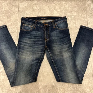 Blå jeans från Nudie Jeans - Snygga blå jeans från Nudie Jeans med klassisk femficksdesign och orangea kontrastsömmar. Jeansen har en lätt tvättad look och raka ben. Tillverkade i slitstarkt bomullstyg och passar perfekt till en avslappnad stil.