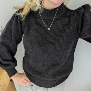 Svart stickad tröja med puffärm - Svart stickad tröja med högt ribbat halslinne och snygga puffärmar. Tröjan har en loose passform och är perfekt för kyligare dagar. Mjukt material och ribbade muddar vid ärmslut och nederkant. Enkel att styla till både jeans och kjol.