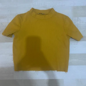 Gul croppad topp med kort ärm - En enkel och stilren gul croppad topp med korta ärmar och hög hals. Toppen är ribbad och har rå kant nertill för en avslappnad vibe. Perfekt att matcha med jeans eller kjol för en cool look.