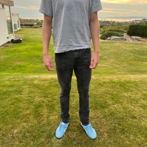 Svarta Nudie jeans - Säljer ett par svarta skinny jeans med klassisk femficksdesign och smal passform. Jeansen har normal midja och är tillverkade i stretchigt jeansmaterial för en bekväm känsla. Perfekta för dig som gillar en stilren och enkel look. Märket är Nudie och nypris är runt 1500kr