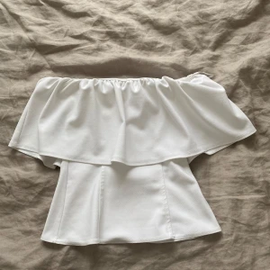 Vit bandeau tubtopp från Zara - Superfin vit bandeau tubtopp från Zara med volang upptill. Toppen är axelbandslös och har en snygg, figurnära look. 