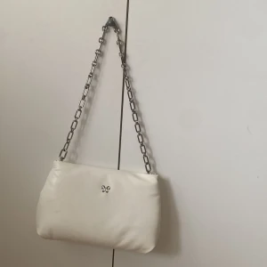 Vit axelväska med kedja från Wera - Snygg vit axelväska från Wera med stilren design och silverfärgad kedja som axelrem. Väskan är gjord i mjukt skinn och har ett ljust innerfoder med både dragkedjefack och öppen ficka. Perfekt för att lyfta vilken outfit som helst.