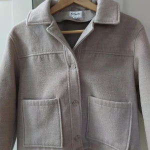 Beige jacka från Kappahl - Säljer en beige jacka från Kappahl i mjukt material. Jackan har klassisk krage, stora framfickor och knäppning med knappar framtill. Ser nopprig ut på bilden men de har den inte längre.  