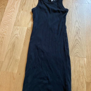 Svart ribbad tajt klänning  - Svart långklänning från H&M i storlek XS. Klänningen är ribbad och ärmlös med rund halsringning. Enkel och stilren design som sitter snyggt och är lätt att matcha med accessoarer. 
