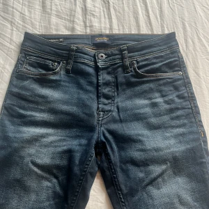 Mörkblå jeans från Jack & Jones 27/32 Slim straight - Snygga mörkblå jeans från Jack & Jones med klassisk femficksdesign och kontrastsömmar. Jeansen har en rak passform och är tillverkade i stretchig denim för extra komfort. Perfekta till vardags med en cool tvättad look. Priset är förhandlingsbart.