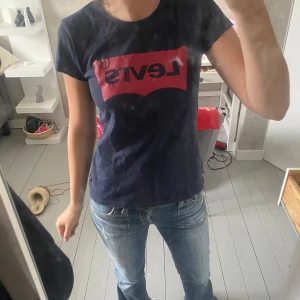 Mörkblå Levi's t-shirt med röd logga - Snygg mörkblå t-shirt från Levi's med klassisk röd logga framtill. T-shirten är kortärmad och har en normal passform. Perfekt till jeans eller shorts för en avslappnad look.