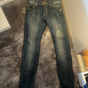Mörkblå skinny jeans Jack & Jones - Säljer ett par mörkblå skinny jeans från Jack & Jones med snygga slitningar och klassiska fem fickor. Jeansen har normal passform i midjan och smalare ben, perfekt för en trendig look. Materialet är tåligt denim med snygga kontrastsömmar. Storlek 29:30