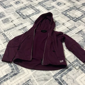 Vinröd jacka med huva från Icewear - Säljer en vinröd jacka från Icewear i storlek M. Jackan har huva, dragkedja framtill och två fickor med dragkedja. Perfekt för kyliga dagar och har en sportig look. Materialet känns mjukt och smidigt, och jackan har en enkel, stilren design.