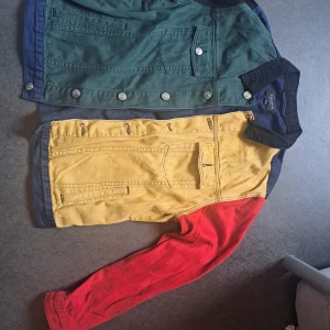 Färgglad jeansjacka från Pacsun - Säljer en unik jeansjacka från Pacsun i storlek M. Jackan har coola färgblock i blått, grönt, gult, rött och svart. Klassisk jeansjacke-modell med knappar framtill, bröstfickor och långärmade ärmar. Perfekt för dig som vill sticka ut med din stil.