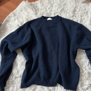 Mörkblå stickad tröja från H&M - En enkel och stilren mörkblå stickad tröja från H&M. Tröjan har rund halsringning och långa ärmar, perfekt för lager på lager. Mjuk och skön känsla, passar dig som gillar en klassisk look.