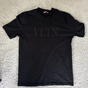 Svart VLTN t-shirt från Valentino - Svart t-shirt från Valentino med VLTN-tryck på bröstet. Klassisk rund hals och korta ärmar. Tillverkad i mjuk bomull som känns skön mot huden. Snygg och stilren design som passar perfekt till jeans eller shorts.