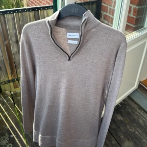 Grå merinoulltröja half zip These Glory Days - Snygg långärmad tröja från These Glory Days i mjuk merinoull. Tröjan har en stilren half zip-dragkedja vid kragen och en clean, minimalistisk look. Perfekt för lager-på-lager och funkar året runt. Klassisk passform och riktigt skön känsla.