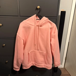Ljusrosa hoodie stl S - Säljer en ljusrosa hoodie med huva och dragsko i stl S. Tröjan har en stor magficka framtill och är tillverkad i mjukt material. Använt max 1 gång.