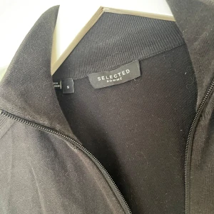 Selected Homme Zip tröja - Svart kofta från Selected Homme i storlek S. Stilren modell med hel dragkedja framtill och ribbade muddar vid krage och ärmslut. Perfekt för lager-på-lager och funkar till många olika outfits. Kom privat för fler frågor och funderingar:)