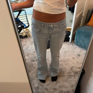 Ljusblå bootcut jeans låg midja - Säljer ett par ljusblå jeans med bootcut och låg midja. De har klassiska fem fickor, bälteshällor och en enkel knappstängning framtill. Jeansen har en chill vibe och är gjorda i mjukt denimtyg som sitter snyggt över höfterna och faller rakt ner mot fötterna.