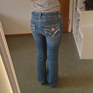 Blå bootcut jeans Gina Tricot 164 - Snygga blå jeans från Gina Tricot i bootcut-modell med låg midja (beror på hur dom sitter man kan också räknas som mid waist). Jeansen har coola detaljer med broderier och paljetter på bakfickorna samt dekorativa knappar. Tillverkade i klassiskt denimtyg som ger en skön passform. Bra längd för mig som är 168cm lång. 