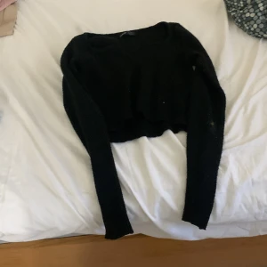 Svart croppad stickad tröja - Svart croppad stickad tröja med lång ärm och rund hals. Tröjan har en loose fit och är perfekt att styla med höga jeans eller kjol. Mjuk och skön, passar dig som gillar en enkel men trendig look.